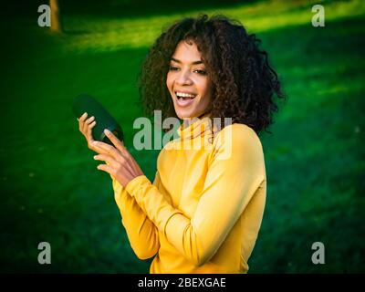 Moderne trendy afroamerikanischen Mädchen hören Musik von drahtlosen tragbaren speaker.Young schöne Frau genießen, tanzen im Park. Stockfoto