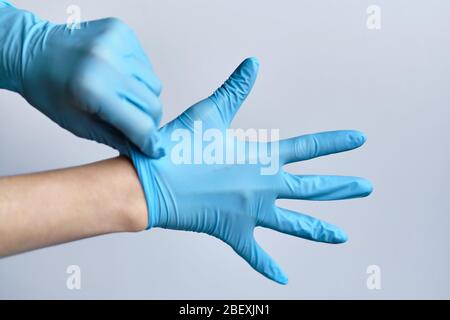Der Prozess des Aufsetzens blauer medizinischer Handschuhe auf die Hände auf einem weißen Hintergrund. Nahaufnahme. Stockfoto