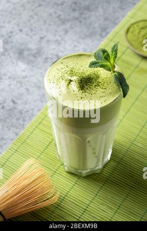 Ein Glas Dalgona Iced Matcha Tee. Geschlagenes weißes Ei mit Matcha-Tee wird der Milch mit Eis hinzugefügt. Vertikales Format. Stockfoto