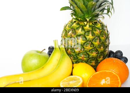 Eine Auswahl an tropischen Früchten vor einem schlichten weißen Hintergrund, darunter eine ganze Ananas, grüner Apfel, Banane, Orange, in Scheiben geschnittene Zitrone und ein Bündel Stockfoto