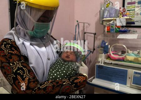 Aceh, Indonesien. April 2020. Eine indonesische Krankenschwester hält ein neugeborenes Baby mit Gesichtsschutz in einem Krankenhaus im Bezirk Bireuen, Provinz Aceh, Indonesien, Donnerstag, 16. April 2020. Tragen von Schutzschilden war Anstrengung zu verhindern, dass die Ausbreitung von Coronavirus Covid-19 . (Foto: Aziz Abdi/INA Photo Agency/Sipa USA) Quelle: SIPA USA/Alamy Live News Stockfoto