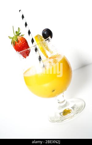 Ein orangefarbener Cocktail-Fruchtgetränk in einem Glas mit einem Partystroh, der auf einem schlichten weißen Hintergrund herabblickt Stockfoto