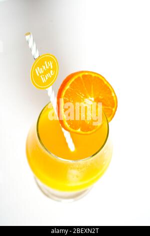 Ein orangefarbener Cocktail-Fruchtgetränk in einem Glas mit einem Partystroh, der auf einem schlichten weißen Hintergrund herabblickt Stockfoto