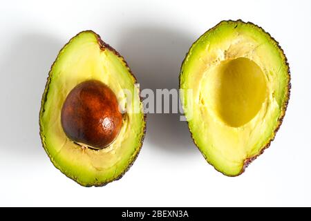 Ein Avocado, das in zwei Hälften geschnitten wurde, um den Kern vor einem weißen Hintergrund zu enthüllen Stockfoto