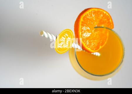 Ein orangefarbener Cocktail-Fruchtgetränk in einem Glas mit einem Partystroh, der auf einem schlichten weißen Hintergrund herabblickt Stockfoto