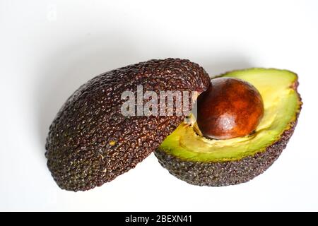 Ein Avocado, das in zwei Hälften geschnitten wurde, um den Kern vor einem weißen Hintergrund zu enthüllen Stockfoto