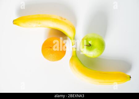 Zwei ganze Bananen an gegenüberliegenden Enden mit einem Apfel und einer Orange gelegt, um ein Muster vor einem schlichten weißen Hintergrund zu erstellen Stockfoto