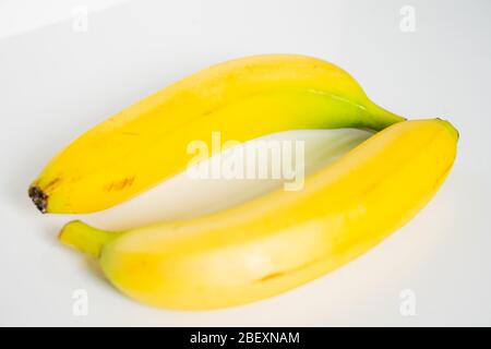 Zwei ganze Bananen an gegenüberliegenden Enden vor einem schlichten weißen Hintergrund gelegt Stockfoto