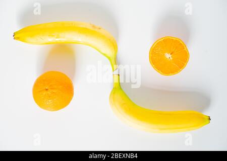 Zwei ganze Bananen an gegenüberliegenden Enden mit zwei orangefarbenen Hälften gelegt, um ein Muster vor einem schlichten weißen Hintergrund zu erstellen Stockfoto