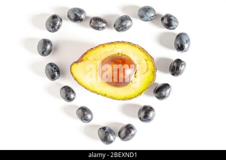 Schwarze Trauben in Form eines Liebesherzens mit einer halben Avocado in der Mitte vor einem schlichten weißen Hintergrund Stockfoto