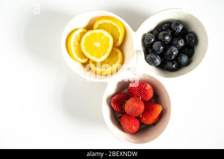 Ein Servierteller mit in Scheiben geschnittenen Zitronen, Erdbeeren und schwarzen Trauben in jedem Segment vor einem schlichten weißen Hintergrund Stockfoto