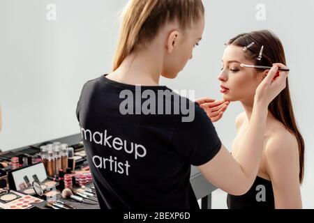 Frau in schwarzem T-Shirt mit Make-up Künstler Schriftzug Lidschatten auf Modell auftragen Stockfoto