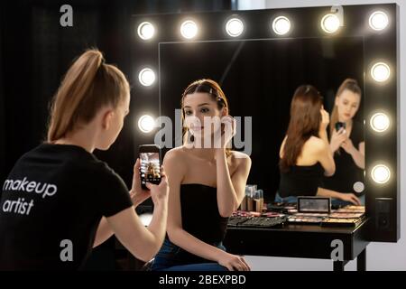 Selektiver Fokus der Frau in schwarzem T-Shirt mit Make-up Künstler Schriftzug, die Foto des Modells Stockfoto