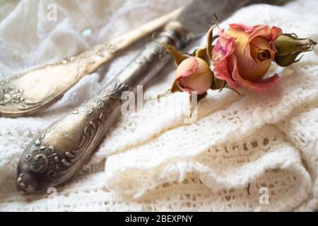 Alte silberne Gabel mit Messer über der weißen Vintage Serviette und trockenen rosa Rosen Stockfoto