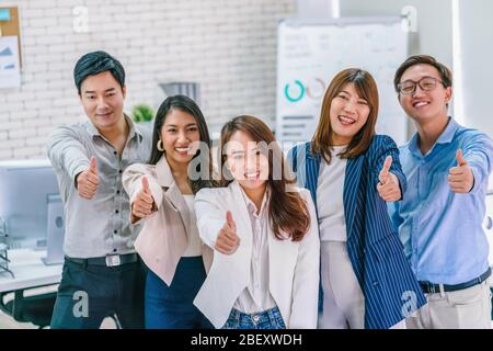 Gruppe von Asian Business People mit Daumen nach oben und Blick auf Kamera zusammen an modernen Arbeitsplatz, Teamarbeit und Teambuilding, Kleinunternehmen Besitzer Stockfoto