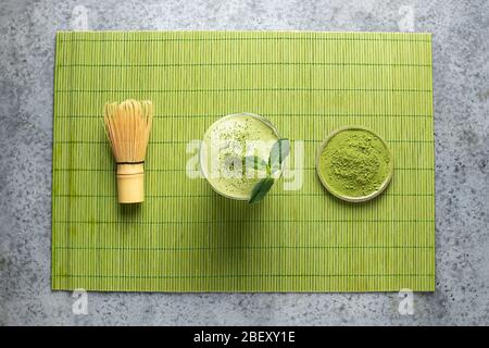 Dalgona Iced Matcha Tee, Bambus Schneebesen und Matcha Pulver auf grüner Matte. Blick von oben. Stockfoto