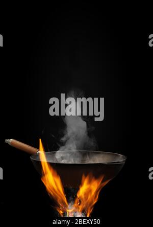 Leere Wok Pfanne mit Rauch über Feuer mit Funken vor schwarzem Hintergrund. Kochkonzept. Mockup, Vorlage für Ihre Collage, Text, Bilder. Nahaufnahme Stockfoto