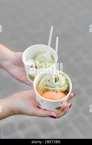 Frauenhände halten Pappbecher mit Eis. Eis Pistazien und Mango Stockfoto