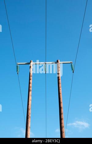 Ein hölzerner Hochspannungsmast mit Glasinisolatoren, die in der britischen Landschaft vor einem blauen Himmel gesehen werden Stockfoto