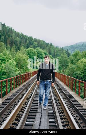 Ein junger Mann in Jeans steht auf einer Eisenbahnstrecke. Bahnhof Stockfoto