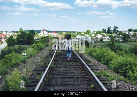 Junge Frau in Jeans und Hemd läuft an einem sonnigen Tag entlang der Bahnstrecke Stockfoto