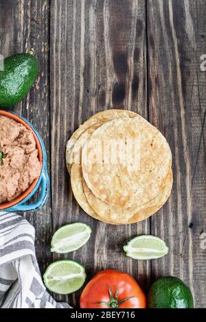 Zutaten aus gebratenen Mais-Tortillas, gebratenen Bohnen, Avocados, Tomaten und frischen Limetten für die Herstellung veganer Tostadas. Draufsicht, Flachlage. Stockfoto