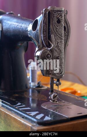 Alte Retro Nähmaschine mit Nadel und eingesteckten weißen Faden. Klemmhebel angehoben. Geringe Schärfentiefe. Konzentrieren Sie sich auf den Pressfuß. Vertikal. Stockfoto