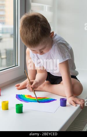 Der Junge, der auf der Fensterbank sitzt, zeichnet den Regenbogen für das Projekt Chasetherainbow Stockfoto