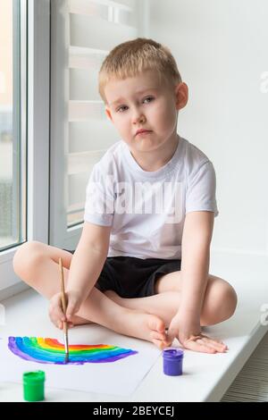 Der Junge, der auf der Fensterbank sitzt, zeichnet den Regenbogen für das Projekt Chasetherainbow Stockfoto