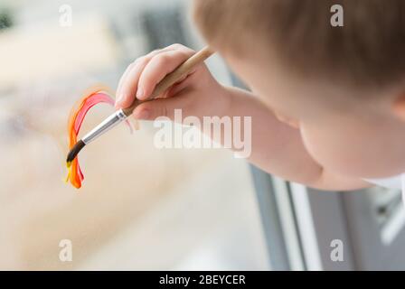 Lasst uns alle gut sein. Kind zu Hause zeichnet einen Regenbogen auf das Fenster. Flash Mob Chasetherainbow auf Selbstisolierung Quarantäne Pandemie Coronavirus. Stockfoto