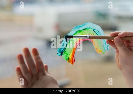 Lasst uns alle gut sein. Kind zu Hause zeichnet einen Regenbogen auf das Fenster. Flash Mob Chasetherainbow auf Selbstisolierung Quarantäne Pandemie Coronavirus. Stockfoto