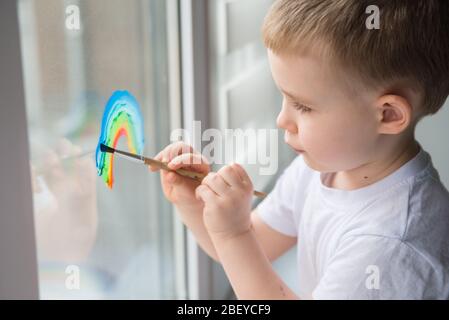 Lasst uns alle gut sein. Kind zu Hause zeichnet einen Regenbogen auf das Fenster. Flash Mob Chasetherainbow auf Selbstisolierung Quarantäne Pandemie Coronavirus. Stockfoto