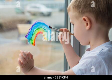 Lasst uns alle gut sein. Kind zu Hause zeichnet einen Regenbogen auf das Fenster. Flash Mob Chasetherainbow auf Selbstisolierung Quarantäne Pandemie Coronavirus. Stockfoto