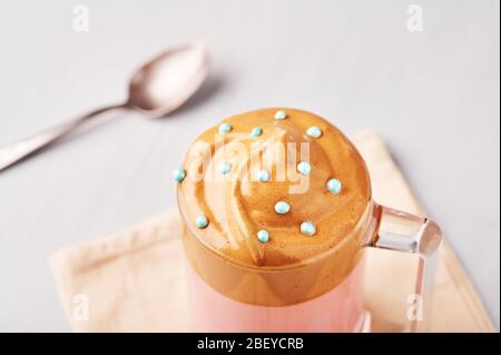 Pink Milk Dalgona Kaffee mit blauen Ostern Streusel in einem Glas Tasse auf hellgrauen Hintergrund dekoriert. Dalgona Schaumkaffee ist ein koreanisches Trendgetränk Stockfoto