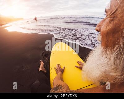 Happy Surfer Senior sitzt auf Surfbrett beobachten Sonnenuntergang Zeit - Reife bärtige Mann mit Spaß am Surfen Tag Stockfoto