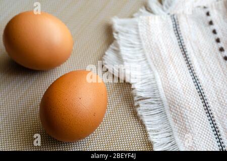 Zwei braune Hühnereier und ein Küchentuch. Nahaufnahme von roh gekochten Bauerneiern auf beige. Ein gefaltetes Handtuch und ein Paar Eier. Ansicht von oben in einem Winkel. Selektiv Stockfoto