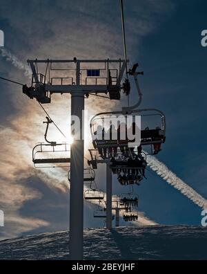 Sessellift mit Skifahrern in der Sonne über einen schneebedeckten Berg im Skigebiet gehen Stockfoto