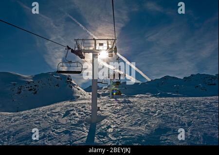 Sessellift mit Skifahrern in der Sonne über einen schneebedeckten Berg im Skigebiet gehen Stockfoto