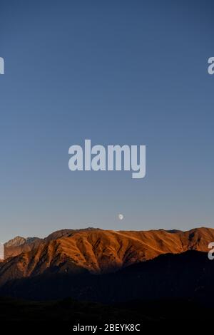 Kaukasus, Georgien, Tusheti Region, Omalo. Der Mond steigt über einem Berg auf, der von der untergehenden Sonne in der Region Tusheti erleuchtet wird. Stockfoto