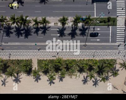 Top-down-Luftaufnahme des Ipanema Boulevard mit Autos vorbei an der Allee von Palmen und Fußgängerüberweg mit Menschen Radfahren und Wandern flankiert Stockfoto