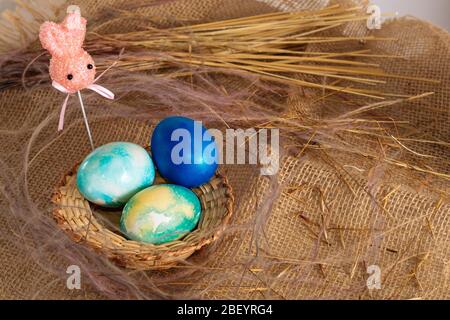 Mehrfarbige Ostereier in Blautönen und Osterhasen auf einem Stock auf einem braunen Stoffhintergrund. Stockfoto
