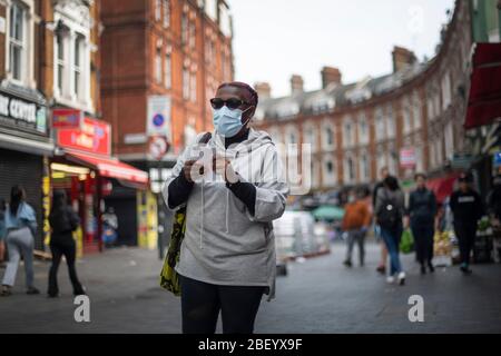 Eine Frau in einer schützenden Gesichtsmaske geht durch den Brixton Market in South London, während Großbritannien weiterhin in der Lockdown-Richtung bleibt, um die Ausbreitung des Coronavirus einzudämmen. Stockfoto