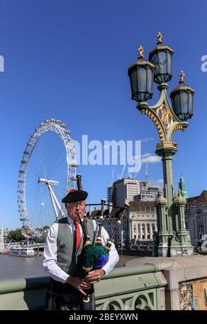 Ein Piper spielt traditionelle Dudelsäcke auf der Westminster Bridge mit dem London Eye im Hintergrund, London, Großbritannien Stockfoto