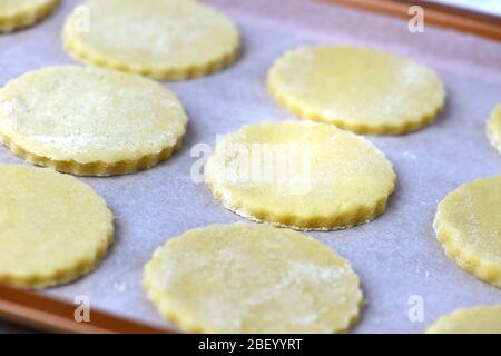 Ungekochte hausgemachte Kekse warten auf den Ofen auf einer Trägerplatte. Aufnahme im Hintergrund mit selektivem Fokus, um Rezept-Overlay hinzuzufügen Stockfoto