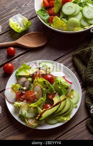 Frischer Frühlingssalat mit Salat, Gurke, Kirschtomaten, Radieschen, Frühlingszwiebeln und Avocado, gekrönt mit Balsamico-Glasur und nativem Olivenöl extra. Stockfoto