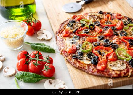 Hausgemachte Pizza mit Kirschtomaten, Salami, Champignons, schwarzen Oliven und Käse auf Holztisch. Stockfoto