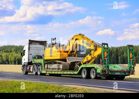 White Scania Sattelschlepper LKW schleppt Komatsu PC 210 LC mittlere Größe Bagger entlang der Straße an schönen Tag des Sommers. Jokioinen, Finnland. Juli 28, 2019. Stockfoto