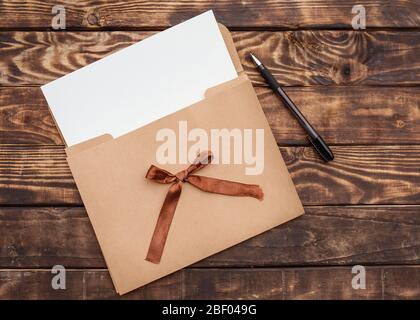 Ein Handwerks-Umschlag, weißes Papier in ihn und schwarzer Bleistift auf alten braunen Holztisch Stockfoto