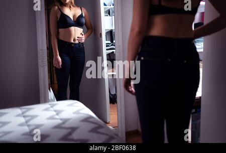 Schlanke Frau, die in den Spiegel schaut. Gewichtsverlust und Ernährung. Hand auf dem Bauch haltend. Stress und Sorgen über die Fettaufnahme. Essstörung. Stockfoto