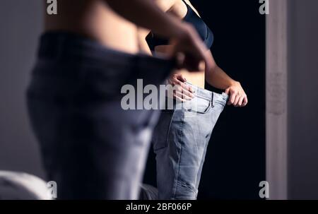 Gewichtsverlust und Diät Erfolg. Skinny gesunde Frau mit schlanken Taille trägt alte große große Hosen. Von Fett bis fit. Im Spiegel schauen. Stockfoto